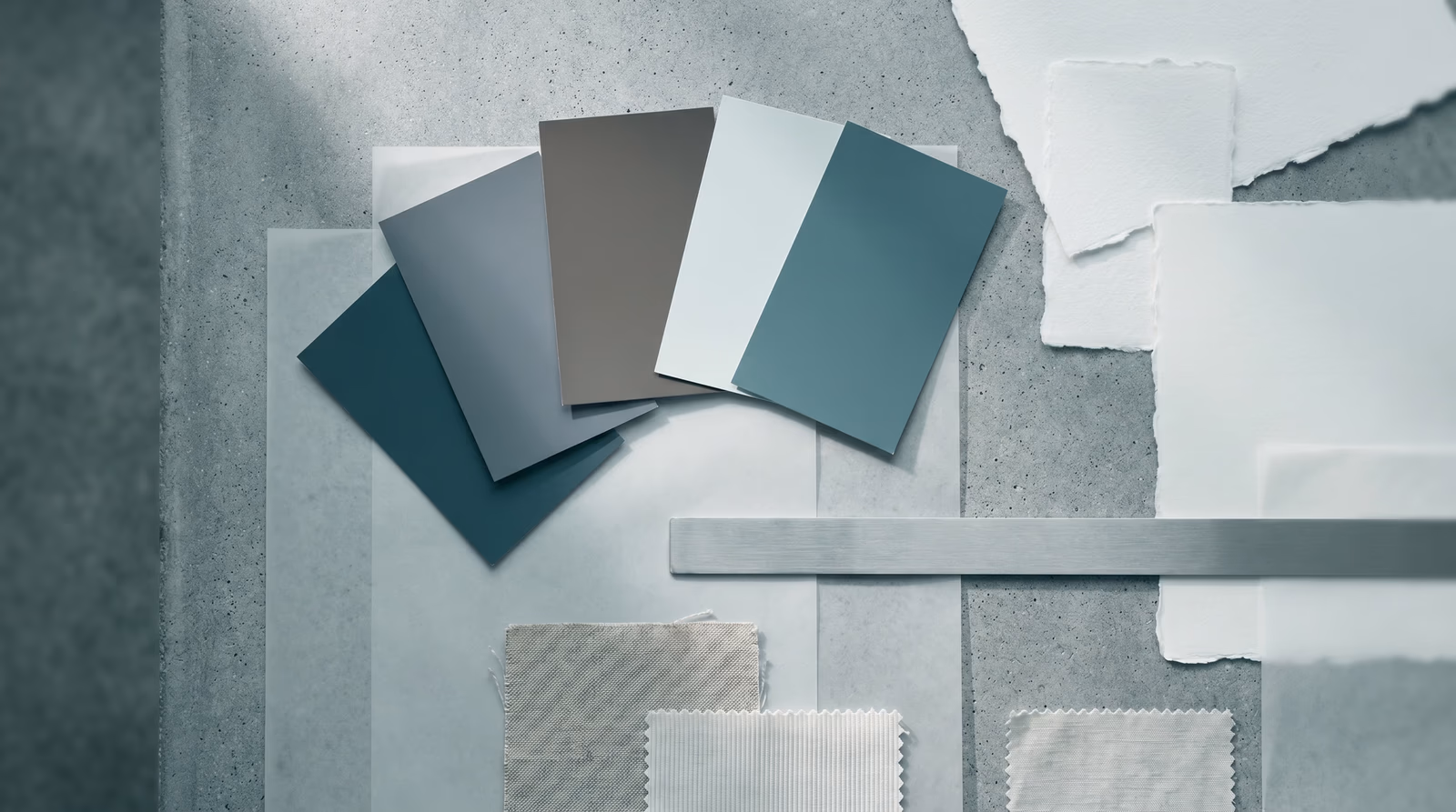Unlabeled color swatches and material texture samples arranged on a cool gray surface, representing the visual elements of a brand design system