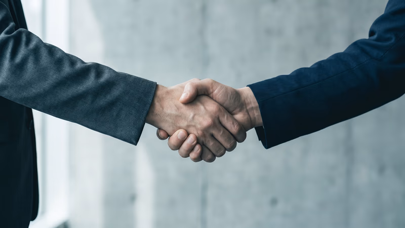 Two hands in a firm professional handshake against a muted concrete wall, symbolizing trust and credibility built through professional web design