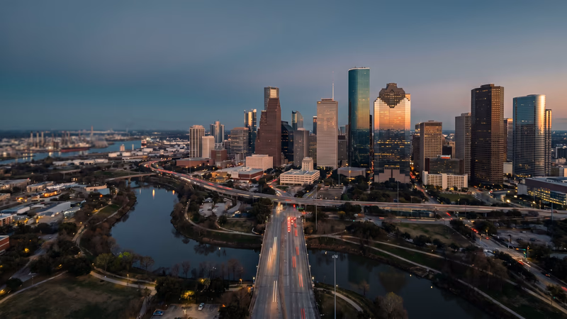 Aerial dusk view of the Houston downtown skyline over Buffalo Bayou with city boulevard light trails, representing the scale and opportunity of the Houston local business market