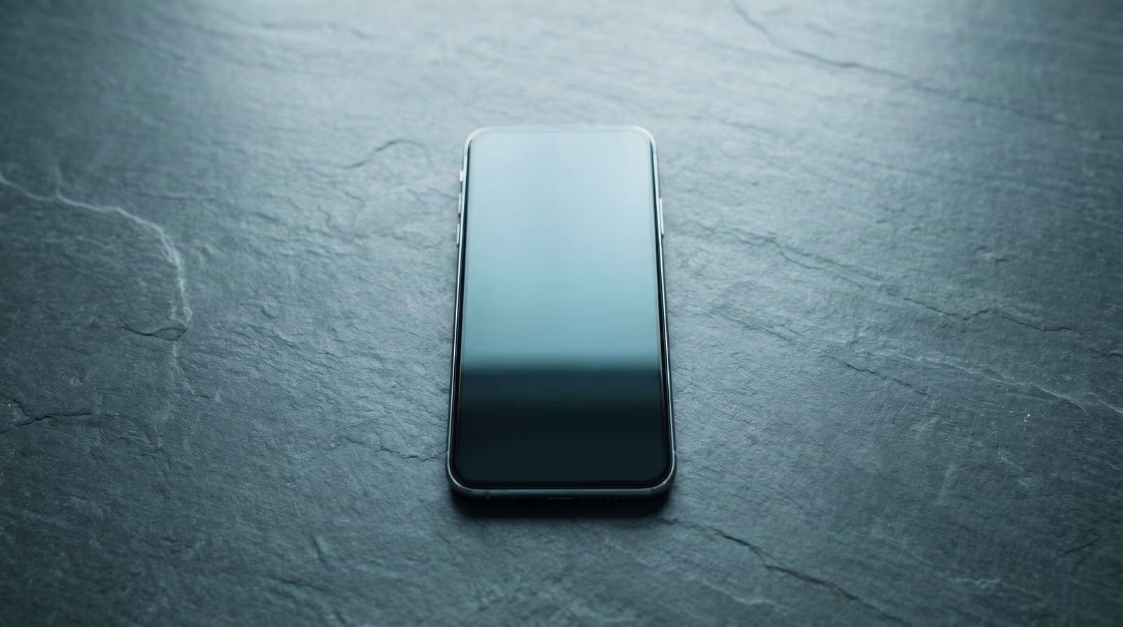 Single modern smartphone in flat-lay with a blank dark screen on a slate surface and generous negative space, representing a mobile-first design philosophy approach