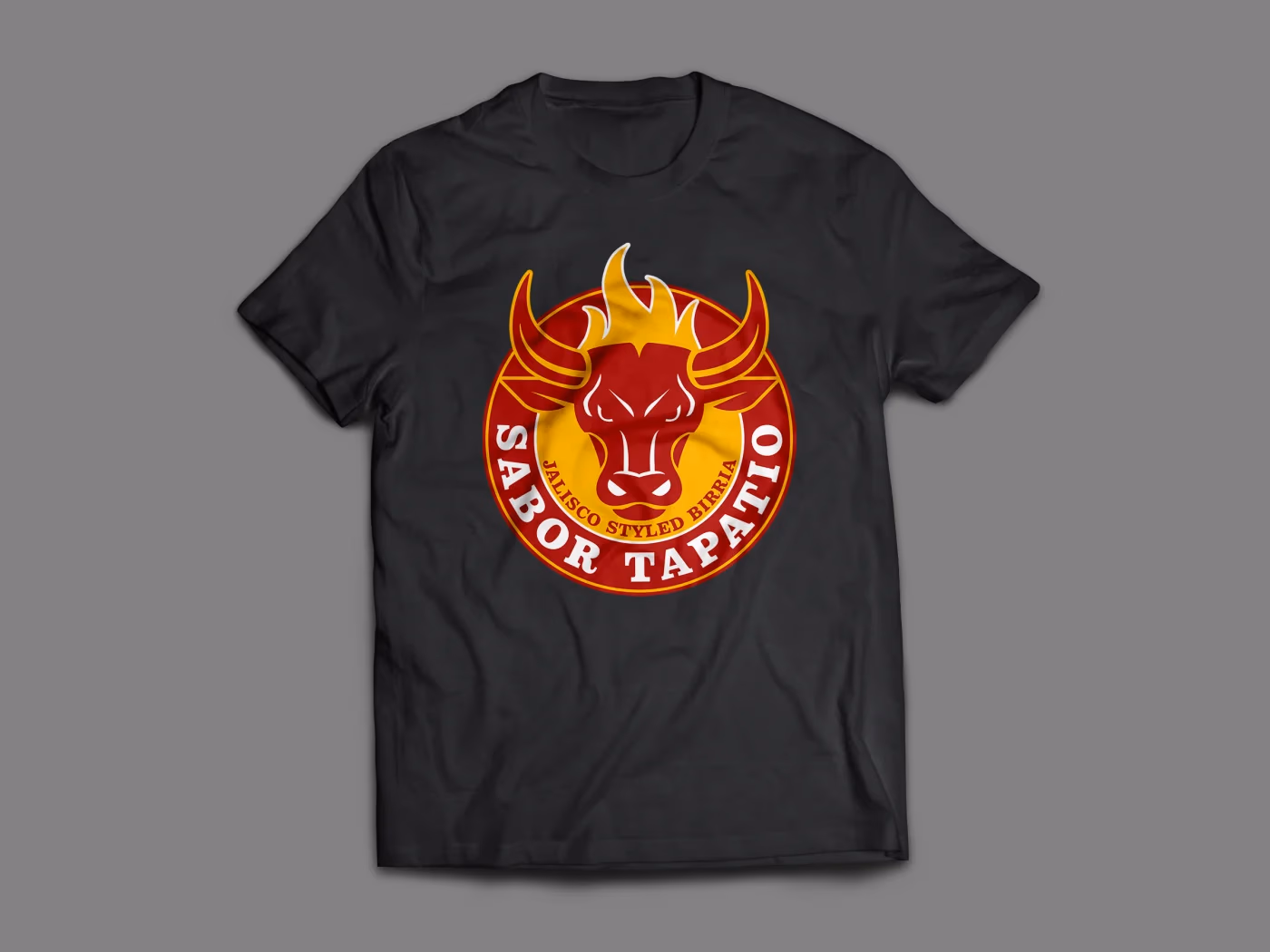 Sabor Tapatio black t-shirt showing the full-color circular bull badge in red and gold on the chest, designed by Desque