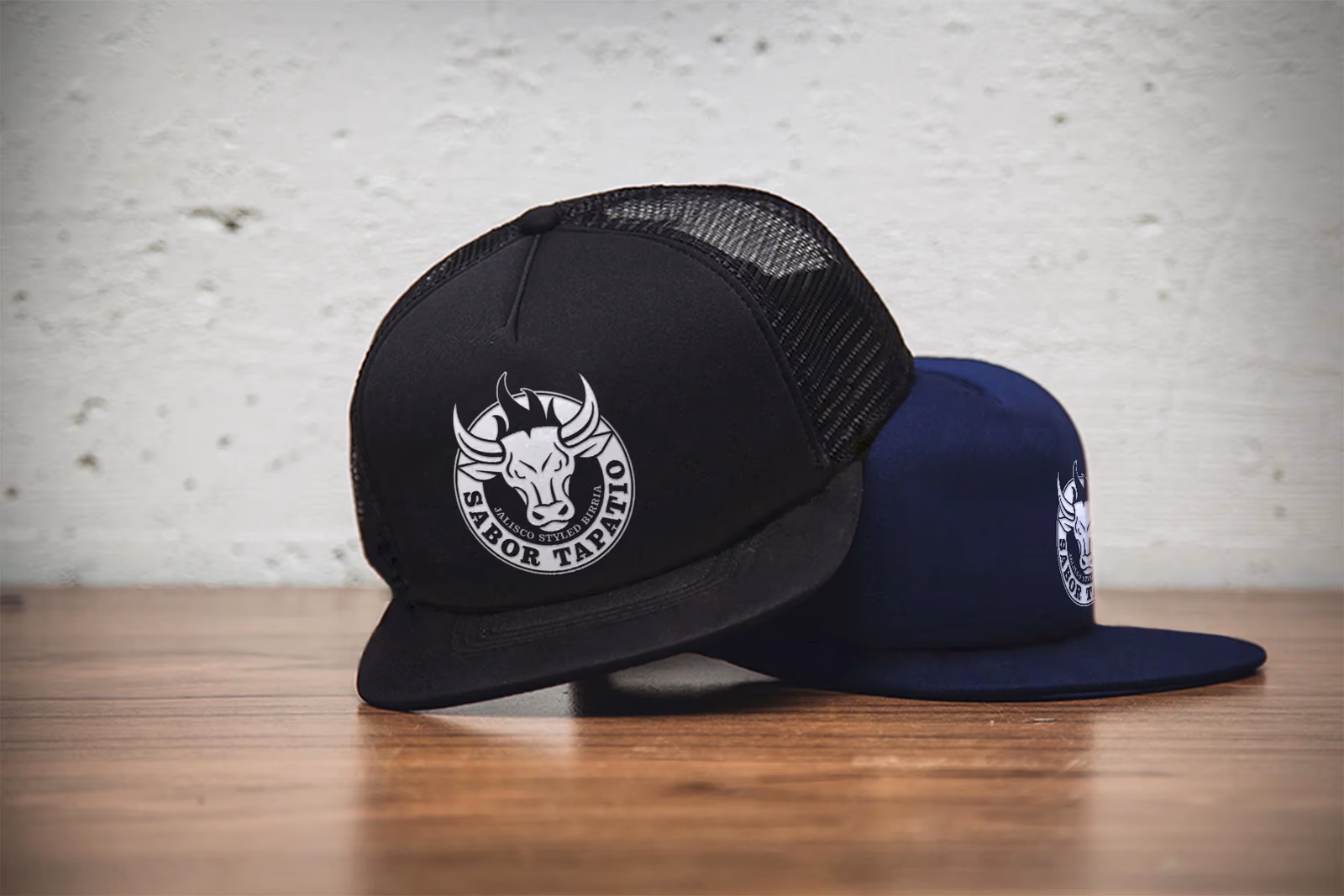 Sabor Tapatio trucker hats in black and navy, showing the circular bull badge logo embroidered on the front panels, designed by Desque