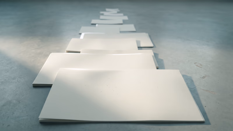 A cascade of blank matte photo prints in descending sizes arranged on a clean studio surface, representing image compression and optimization techniques for web performance