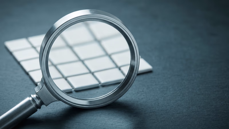A magnifying glass resting over a grid of small blank tiles on a dark slate surface, representing keyword discovery and search analysis