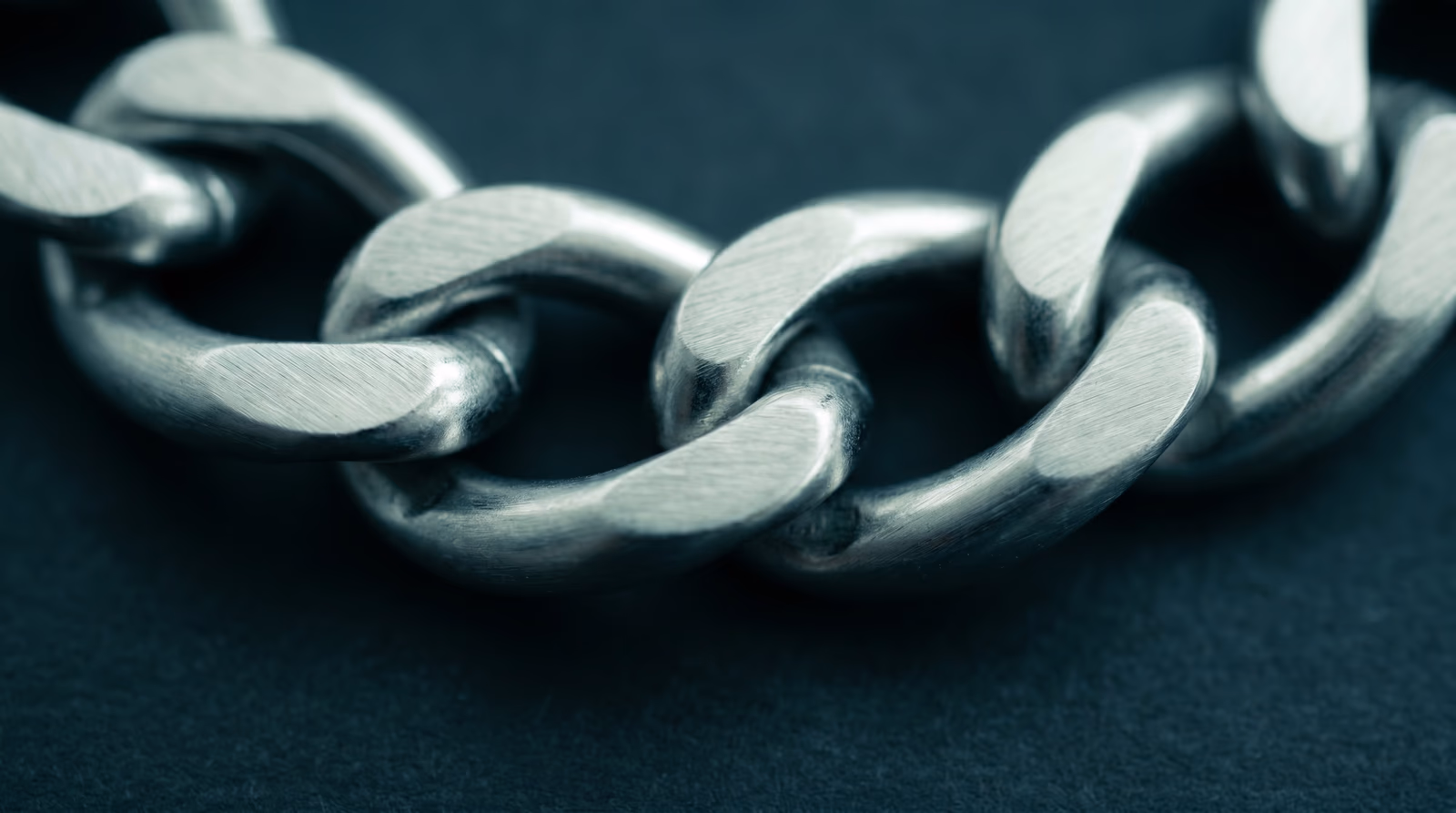 Interlocking brushed-steel chain links under cool directional lighting, representing the interconnected nature of link building and SEO authority
