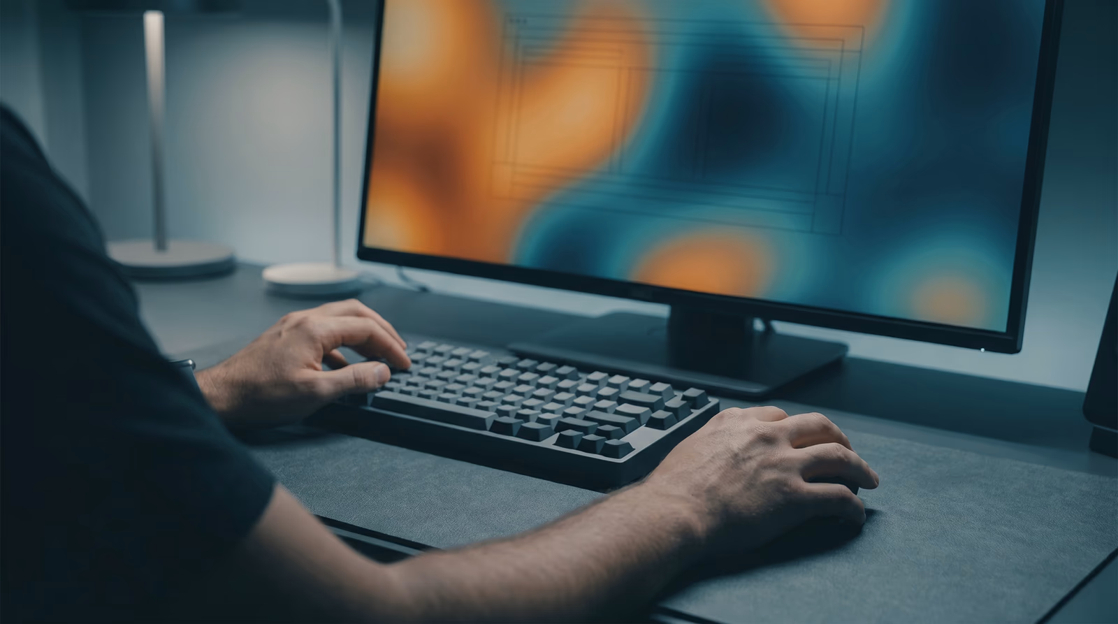Over-shoulder view of hands at a desk with a monitor showing abstract heat-map color blobs over blank wireframe blocks, representing usability testing and user behavior analysis