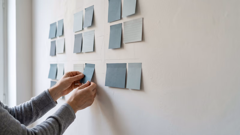 Blank sticky notes and index cards arranged in affinity clusters on a studio wall, representing user research synthesis and qualitative data grouping