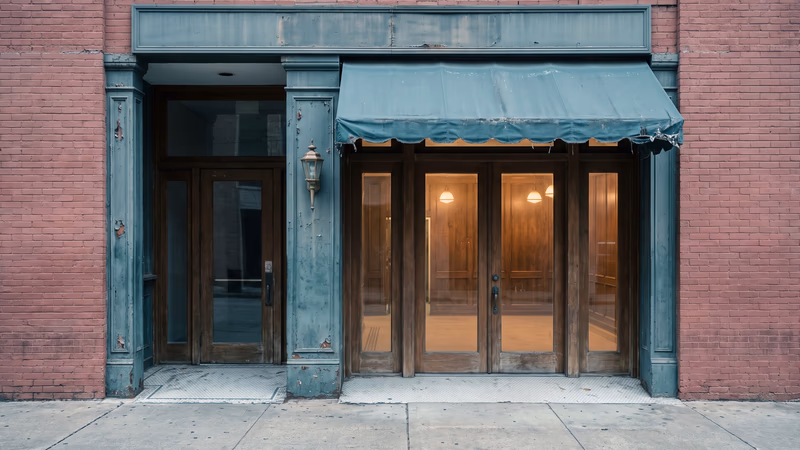 Recessed entrance of an old downtown Houston brick storefront with a faded awning and dusty doors, a warm walnut-paneled interior glowing through the glass