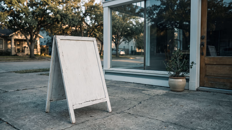 Blank white A-frame sidewalk sign outside a Houston Heights shop at golden hour, its empty faces waiting for the copy the owner has not written yet