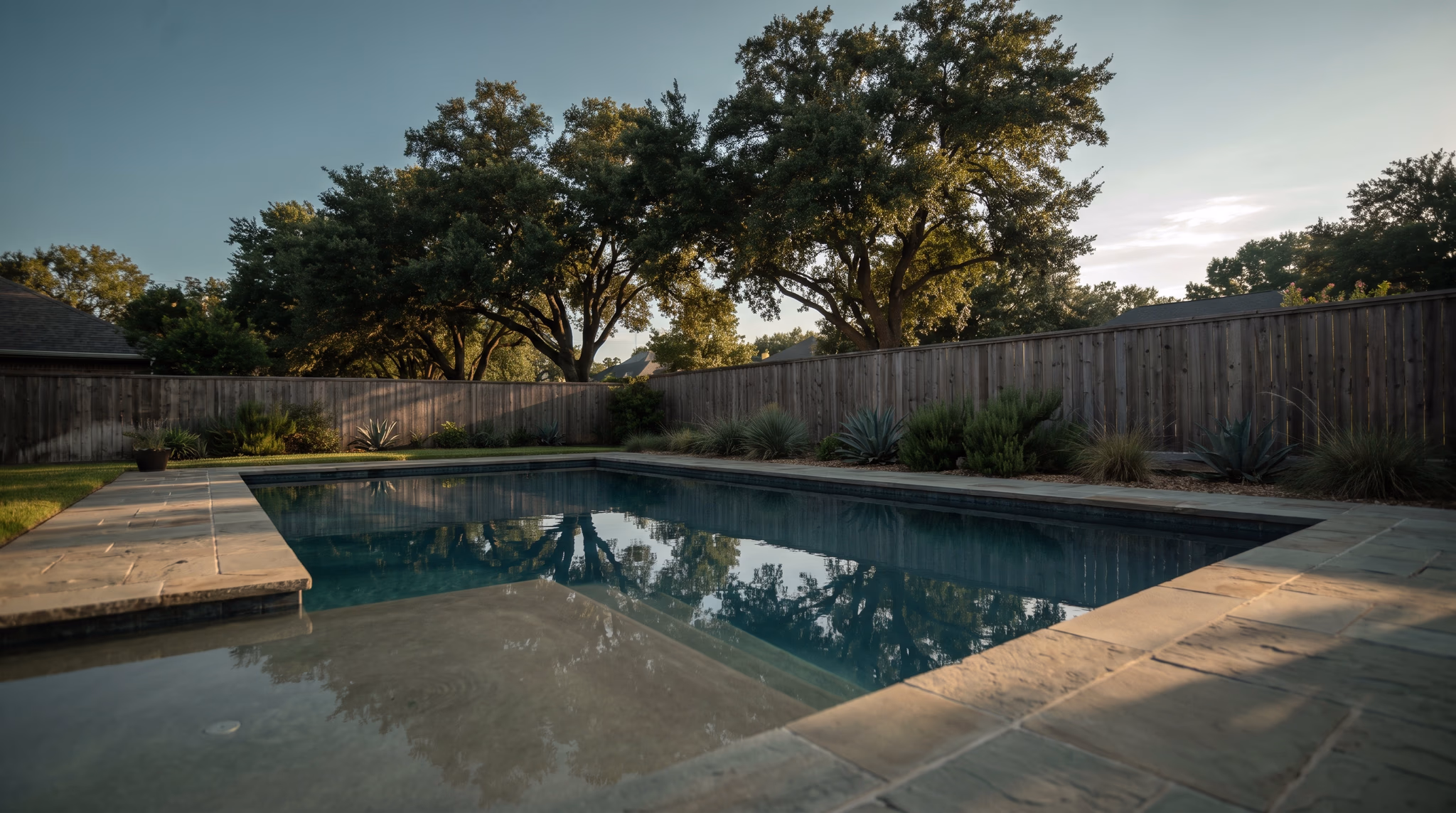 Finished backyard swimming pool at golden hour in west Houston with still water, flagstone coping and live oaks behind it, the finished result a website is built to sell