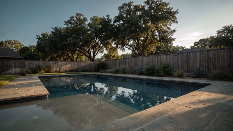 Finished backyard swimming pool at golden hour in west Houston with still water, flagstone coping and live oaks behind it, the finished result a website is built to sell