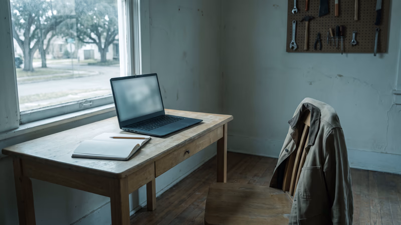 A one-desk back office with a single wooden chair pulled clear of the desk, a work jacket over its back and an open notebook, the staffing question behind ecommerce platform maintenance